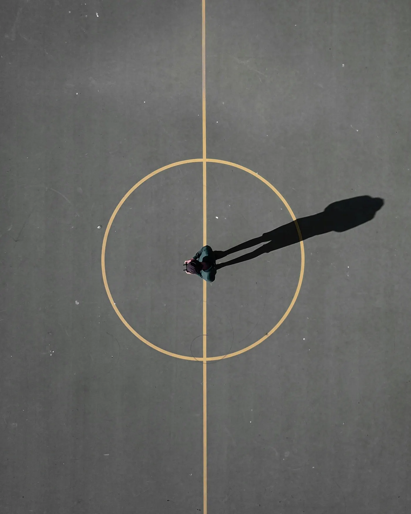Aerial view of a painted circle on a grey court with a single long shadow